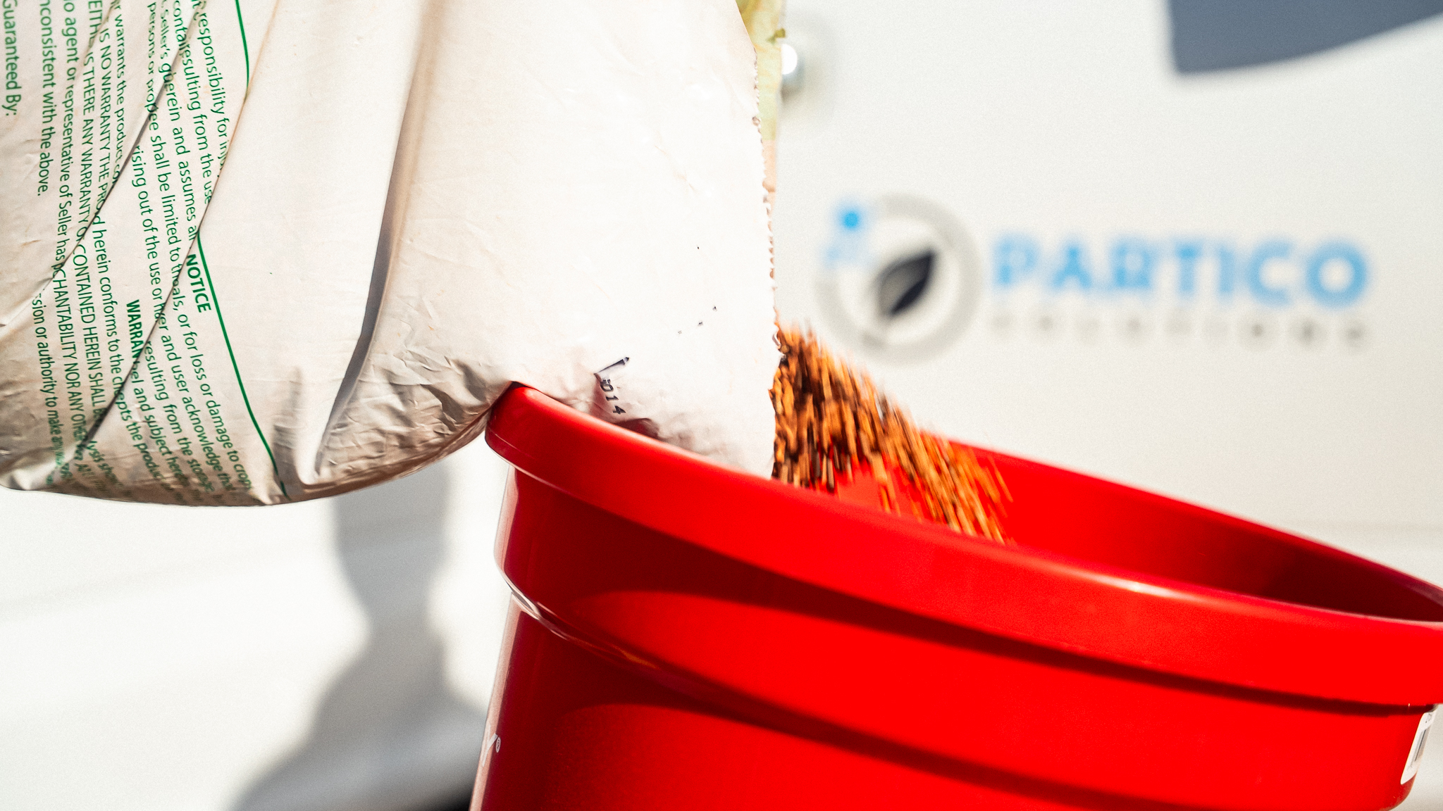 Close-up of a white package with green text being dropped into a bright red trash bin, with shredded packing material spilling over the rim.