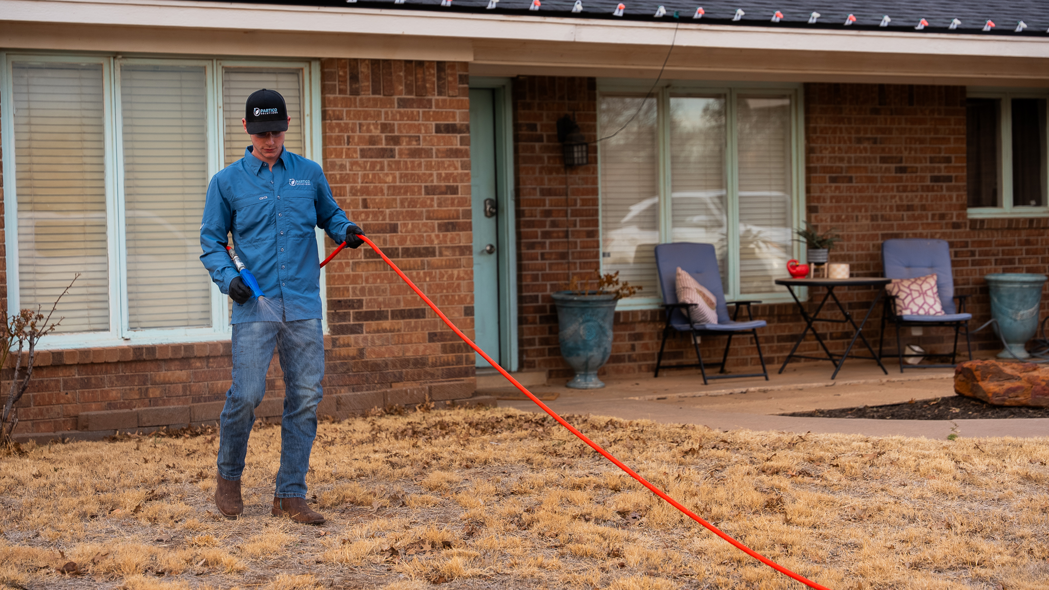 Man in a blue uniform and cap stands on a front lawn, holding an orange extension cord with a blue tool attached.